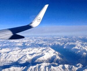 A view of a wing from an airplane flying over snowy mountains. The light spectral quality is very much towards the blue colors.