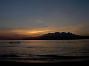 A sunset over the ocean with mountains in the background. The spectral light quality mixes blue, yellow and red light colors.