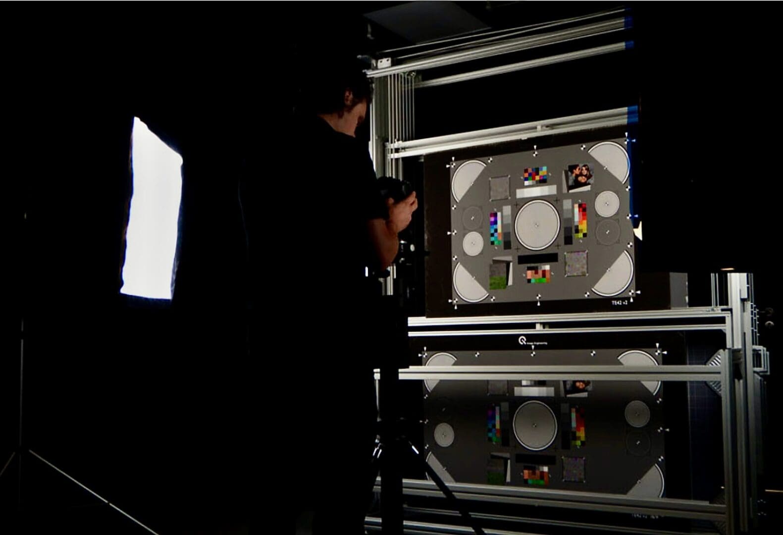 Test engineer taking a picture with a digital camera of a high resolution and color chart target being illuminated by an LED light source programmed to project a CIE standard illuminant.